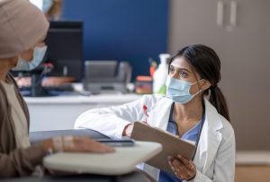 Masked doctor talks with seated patient about blood cancer diagnosis