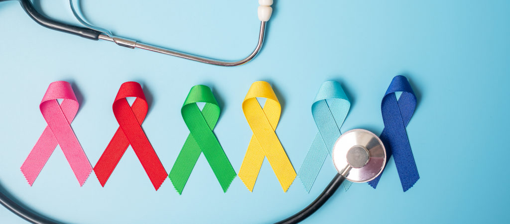 Assorted ribbons corresponding to different types of cancer are arranged in a line next to a stethoscope.