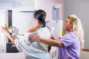 Technician positioning patient at mammography machine in preparation for mammogram