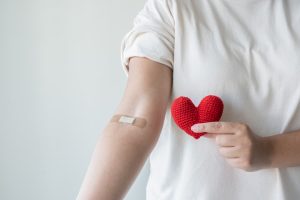 Patient showing Band-Aid on arm while holding red crocheted heart