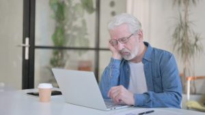 Senior person falling asleep while using laptop at desk