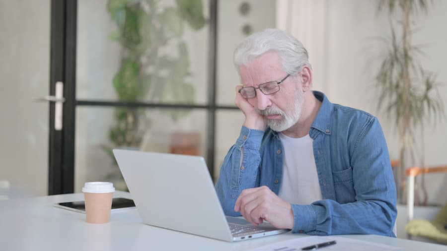 Senior person falling asleep while using laptop at desk