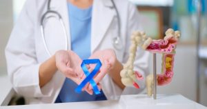 Close-up of doctor’s hand holding blue ribbon with colon model on table