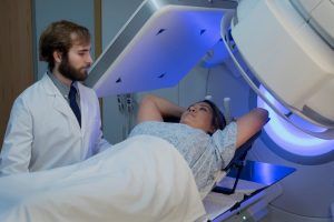 Patient laying on table receiving radiation while doctor stands nearby