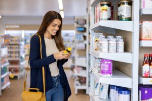 Person in supplement aisle of pharmacy reviewing information on bottle of vitamins