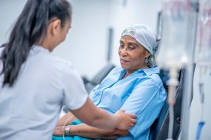 Person wearing head scarf sits for chemotherapy with nurse nearby