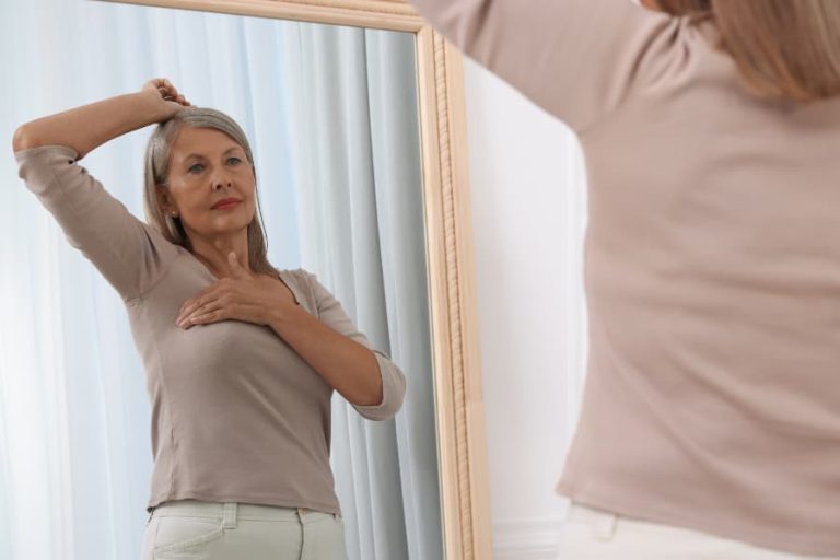 Senior performing breast self-examination in mirror