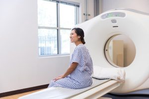Patient in hospital gown sitting by CT scanner