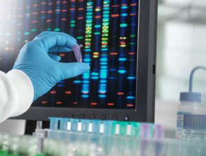Gloved hand of doctor holding up sample next to screen with biomarker testing
