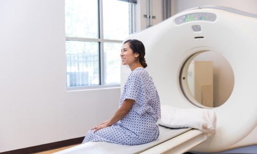 Patient in hospital gown sitting by CT scanner
