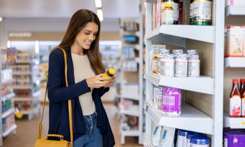 Person in supplement aisle of pharmacy reviewing information on bottle of vitamins